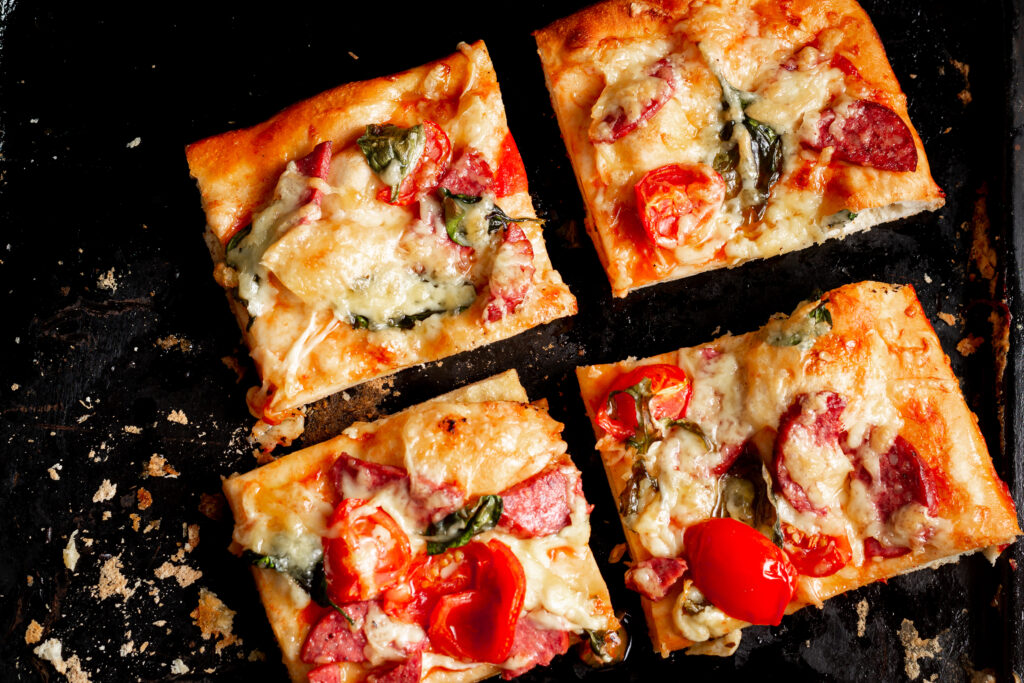 sliced square pieces pizza pie with tomatoes sausage cheese cooked oven black baking sheet x