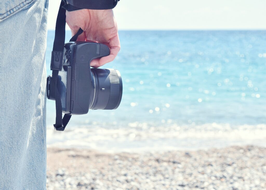 cropped hand man holding camera beach against sky x