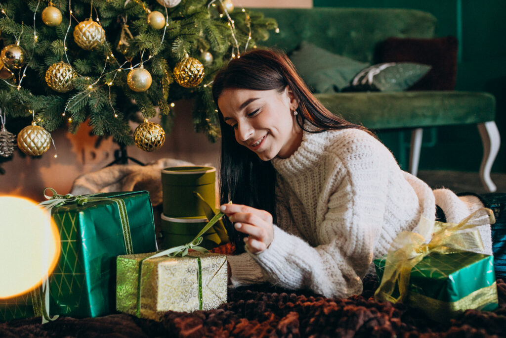young woman by christmas tree unpacking gifts x